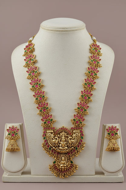 Gold necklace with pink and green stones on a white stand against a beige background