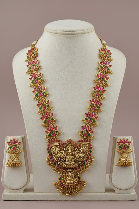 Gold necklace with pink and green stones on a white stand against a beige background