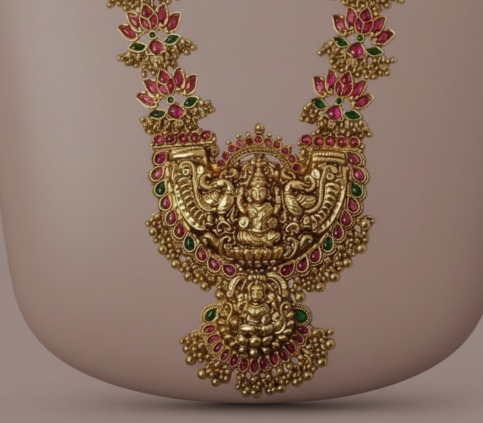 Decorative gold necklace with red and green gemstones on a beige background