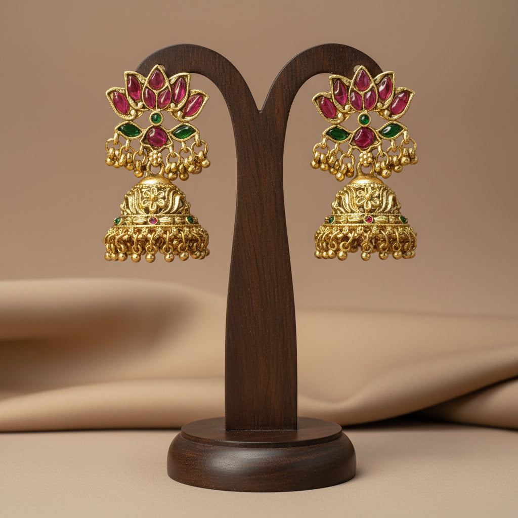 Ornate gold and gemstone earrings held in a hand against a neutral background