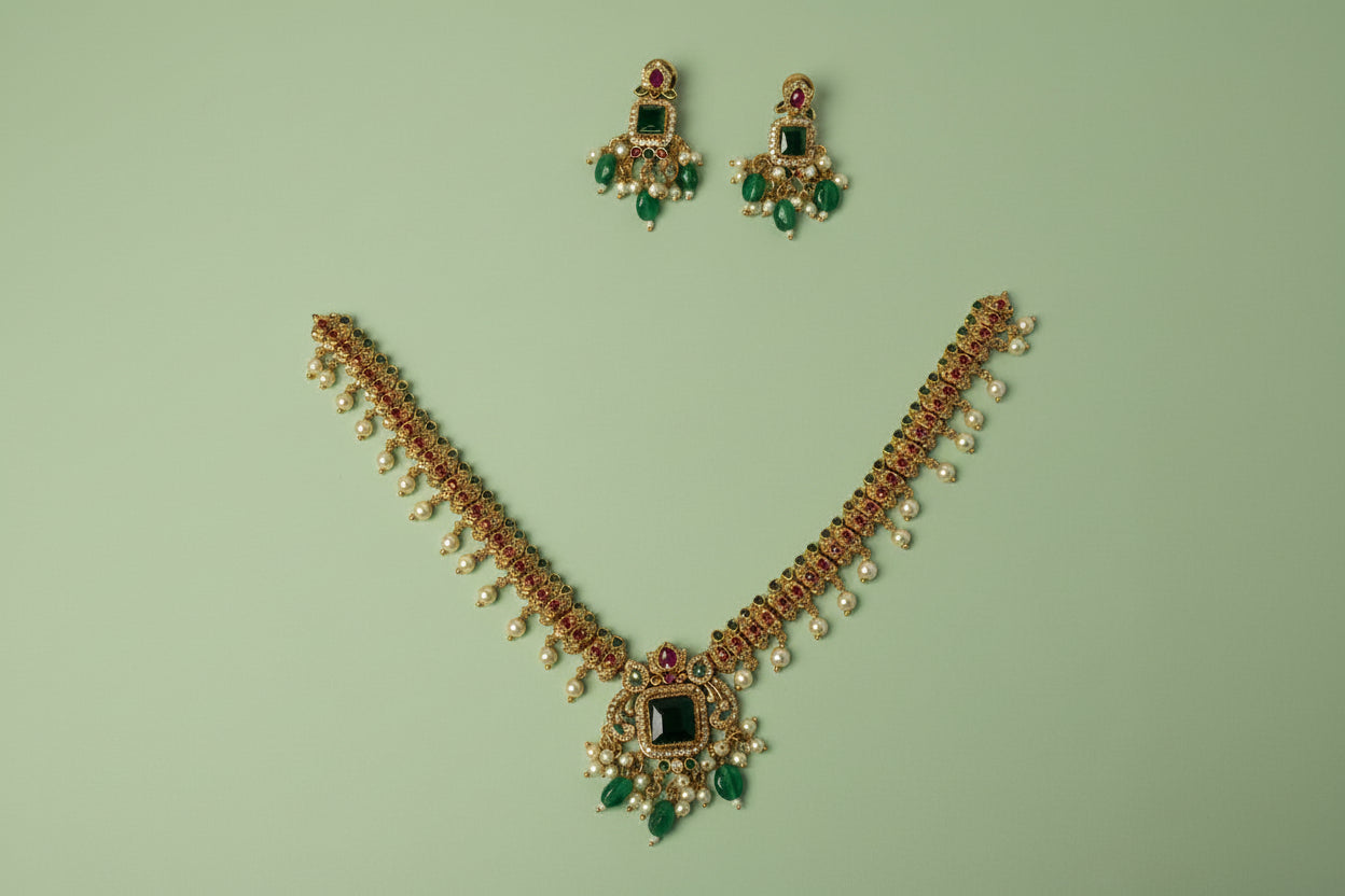 Gold necklace with green and red gemstones on a blue satin background