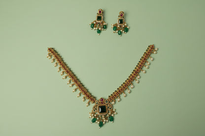 Gold necklace with green and red gemstones on a blue satin background