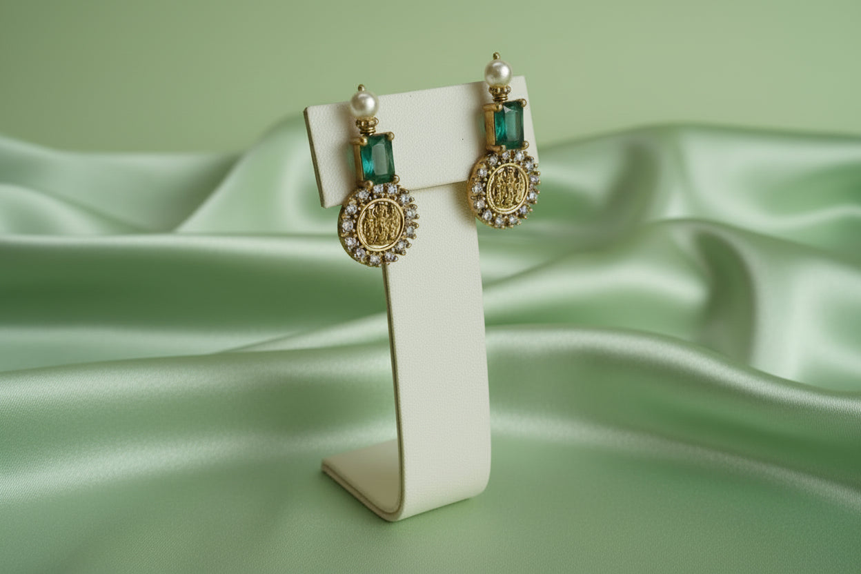 Gold earrings with green gemstones on a white stand against a light green background