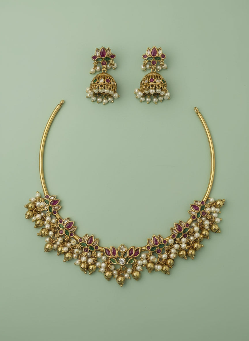 Gold necklace and earrings with red and green gemstones on a light green satin background