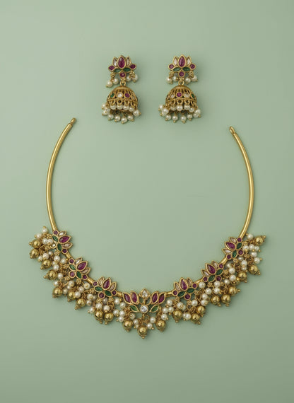 Gold necklace and earrings with red and green gemstones on a light green satin background