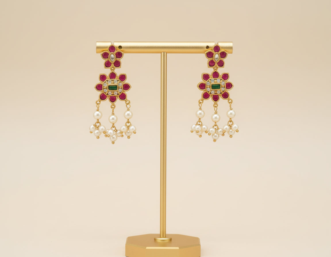 Gold earrings with gemstones and pearls on a gold stand against a beige background