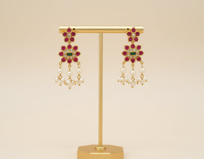 Gold earrings with gemstones and pearls on a gold stand against a beige background