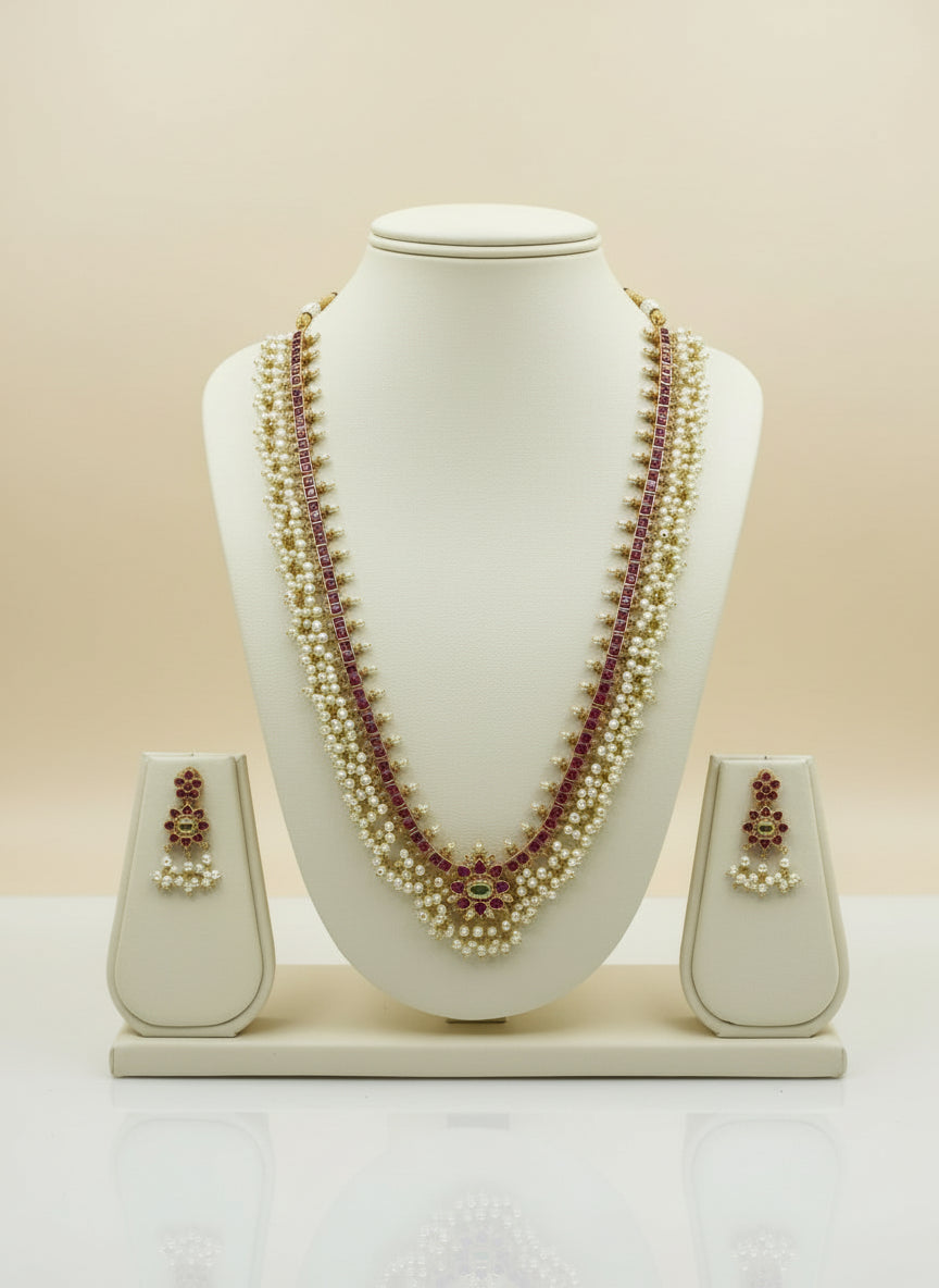 Pearl necklace with red stones and matching earrings on a white mannequin bust against a beige background.