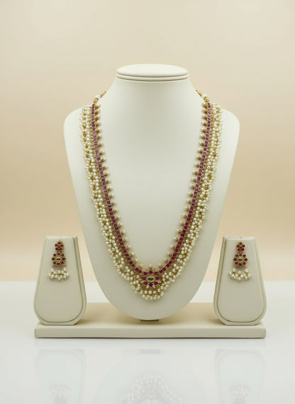 Pearl necklace with red stones and matching earrings on a white mannequin bust against a beige background.