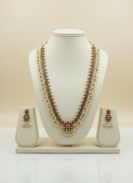 Pearl necklace with red stones and matching earrings on a white mannequin bust against a beige background.