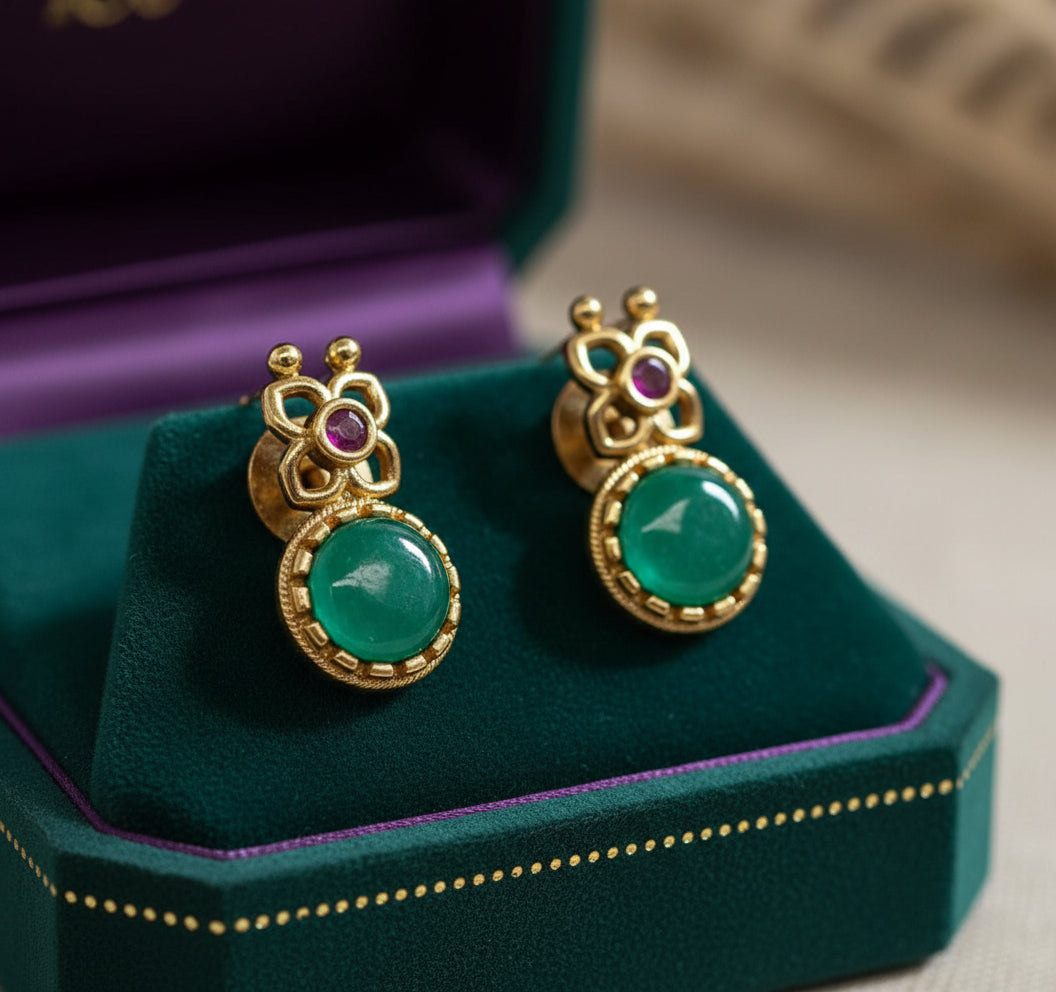 Gold earrings with green stones on a white surface