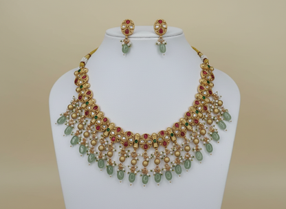 Gold necklace with green and red stones on a mannequin against a cream background