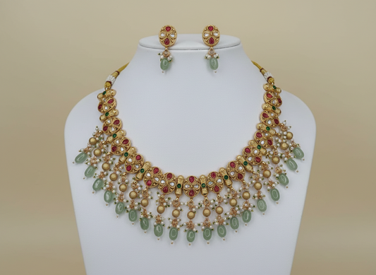 Gold necklace with green and red stones on a mannequin against a cream background