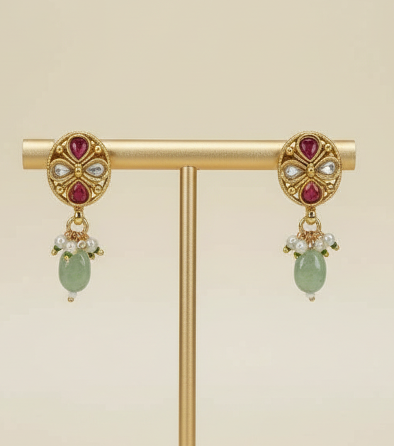 Gold earrings with red gemstones and green beads on a cream background