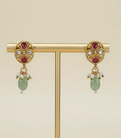 Gold earrings with red gemstones and green beads on a cream background