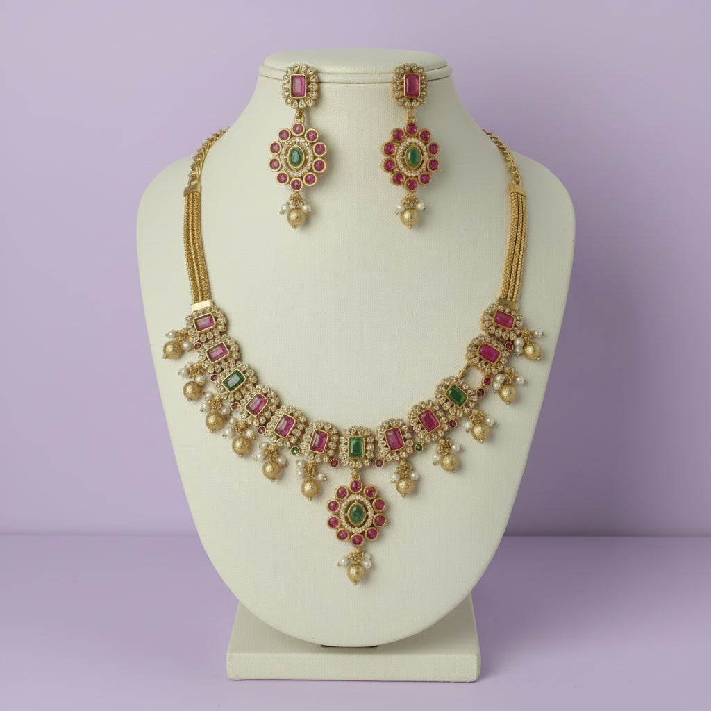 Gold necklace with red and green gemstones on a white background