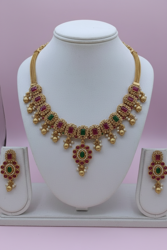 Gold necklace with red and green gemstones on a white stand