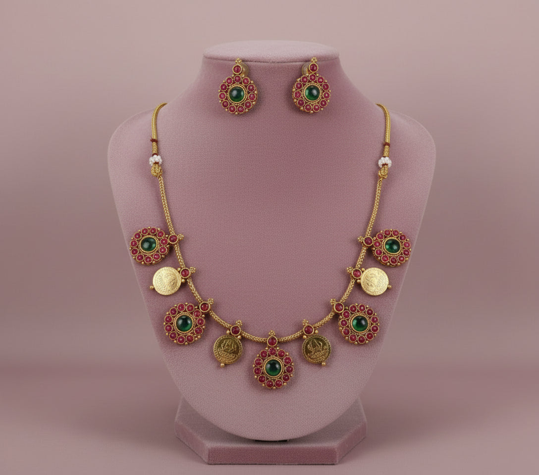 Gold necklace with green gemstones and earrings on a pink stand