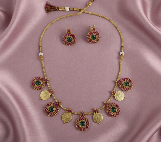Gold necklace with green and red gemstones on a pink satin background
