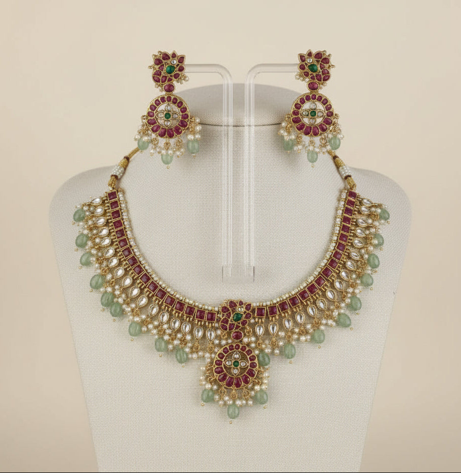 Gold necklace with red and green gemstones on a white background