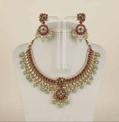 Gold necklace with red and green gemstones on a white background