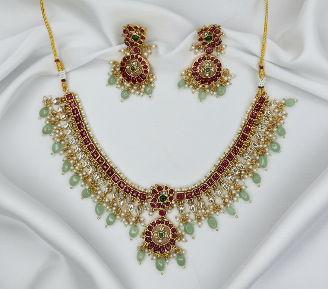 Gold necklace with red and green stones on a gray fabric background