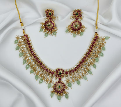 Gold necklace with red and green stones on a gray fabric background