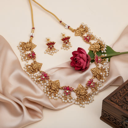 Ornate gold and red jewelry set with a red flower on beige fabric