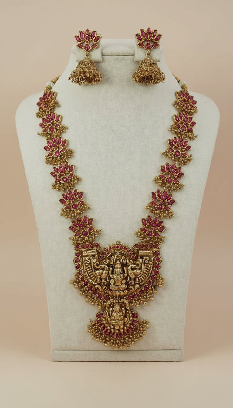 Ornate gold necklace with pink stones on a white stand against a pink background