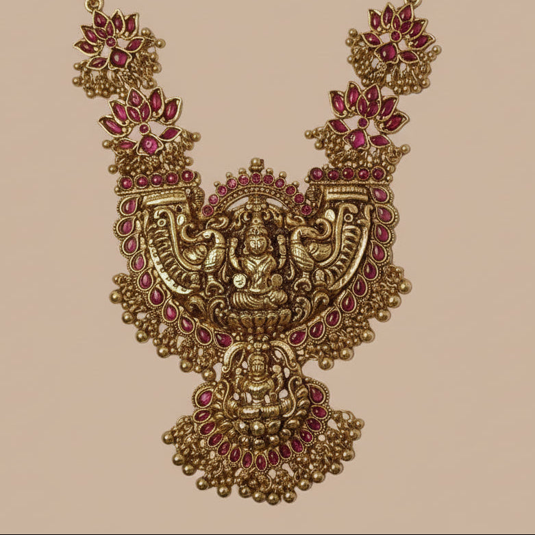 Ornate gold necklace with red gemstones on a pink background