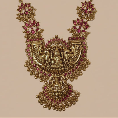 Ornate gold necklace with red gemstones on a pink background