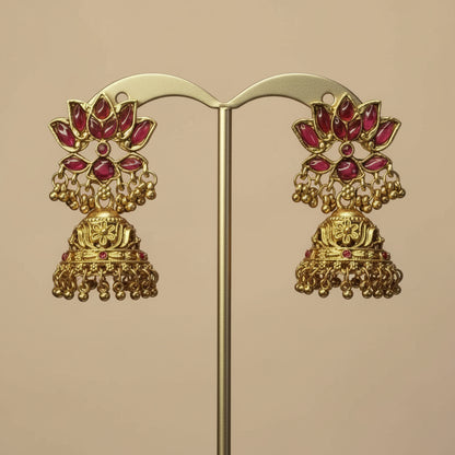 Gold earrings with red stones on a pink background