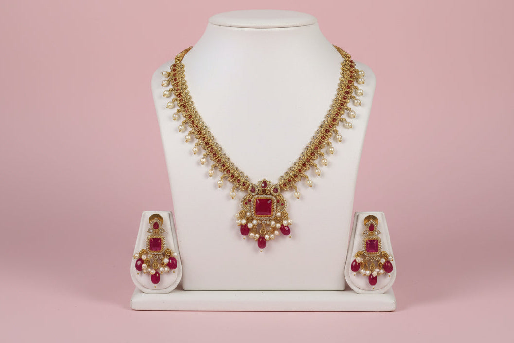 Gold necklace with red gemstones on a mannequin bust against a pink background