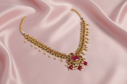 Ornate necklace with gold, red, and pearl details on a light background