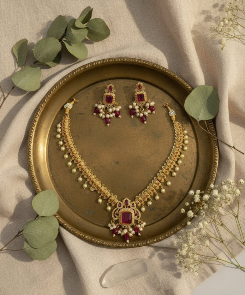 Jewelry set including necklace and earrings on a decorative plate with green leaves and flowers.