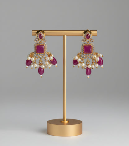 Pair of gold earrings with red stones and pearls on a gold stand against a gray background