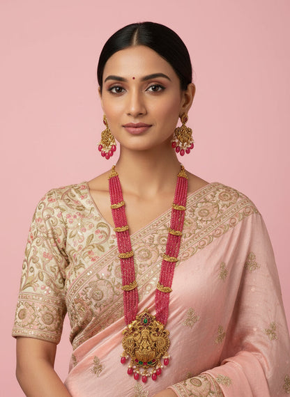 Gold necklace with pink beads and matching earrings on a white fabric background