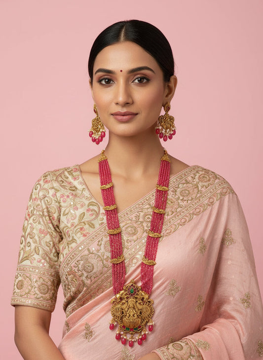 Gold necklace with pink beads and matching earrings on a white fabric background