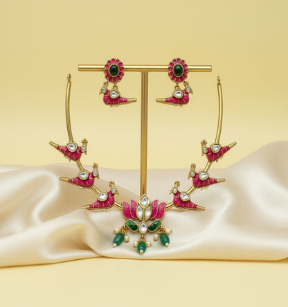 Ornate earrings with pink and green stones on a gold stand against a beige background
