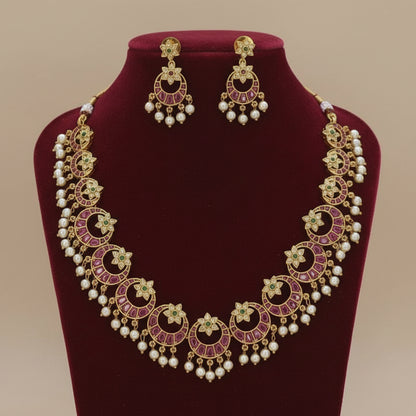 Ornate necklace and earrings set on a red velvet stand with a beige background