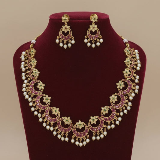 Ornate necklace and earrings set on a red velvet stand with a beige background