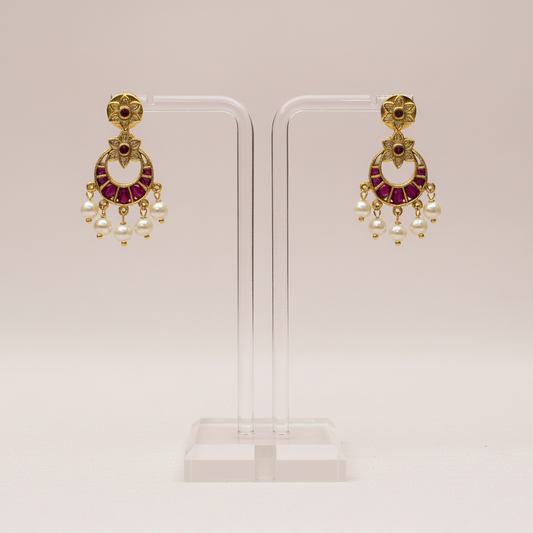 Pair of gold earrings with red and clear stones on a white stand