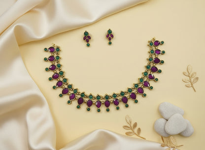 Gold necklace with purple and green gemstones on a beige fabric background