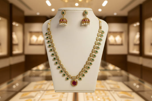 Gold necklace with green gemstones and red stones on a white stand against a beige background
