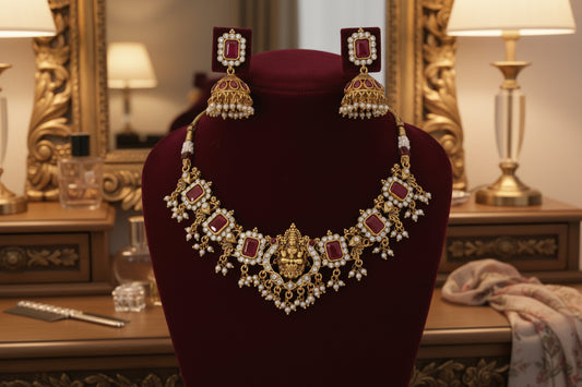 Gold necklace with red stones and matching earrings on a red stand against a gray background