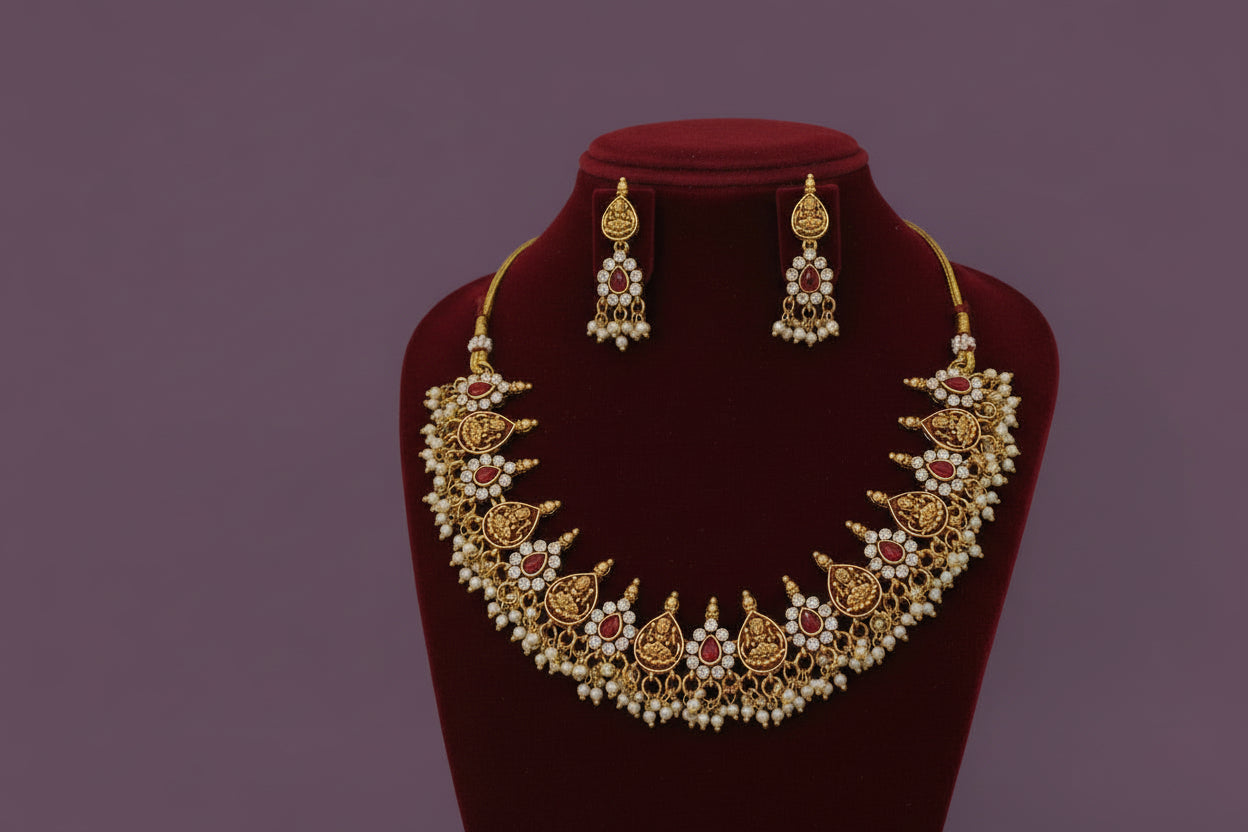 Gold necklace with red and white stones on a red velvet stand against a gray background