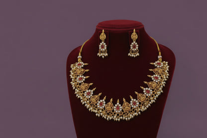 Gold necklace with red and white stones on a red velvet stand against a gray background