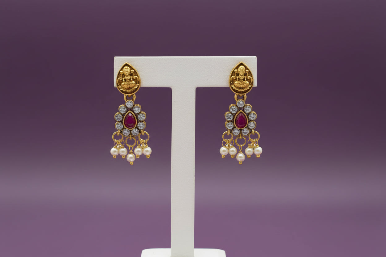 Gold earrings with red gemstones on a white stand against a light purple background