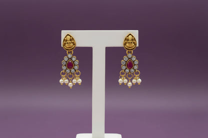 Gold earrings with red gemstones on a white stand against a light purple background