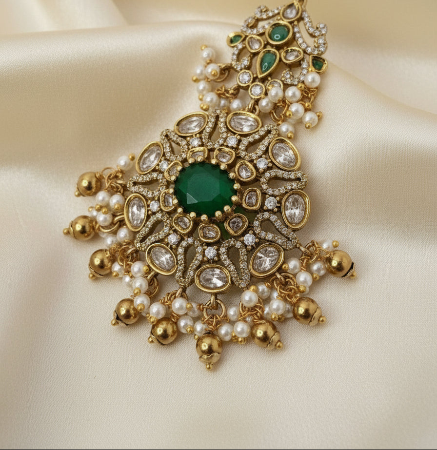 Ornate gold necklace with green gemstone and pearls on a beige fabric background